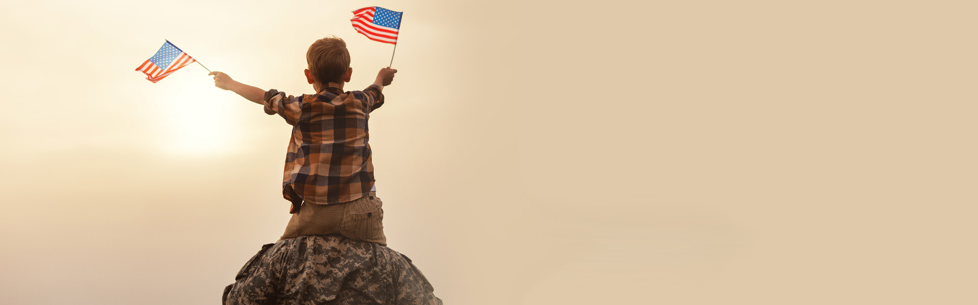 Uniformed solider carrying son on shoulders while boy waves two American flags