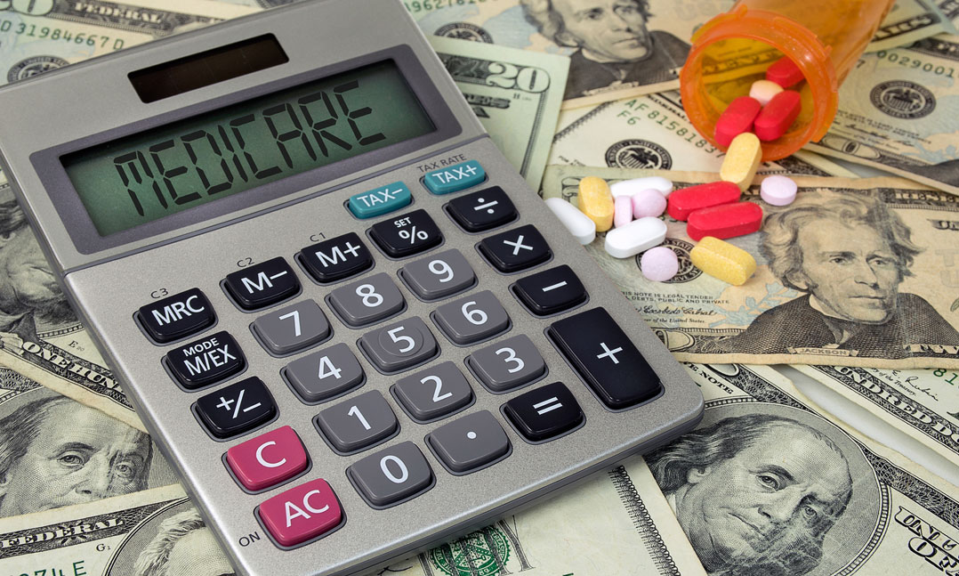 Calculator displaying Medicare and pills from a spilled prescription bottle sit on top of money