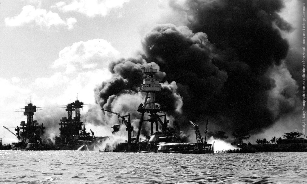 View looking up Battleship Row on 7 December 1941, after the Japanese attack with USS Arizona in the center, burning furiously