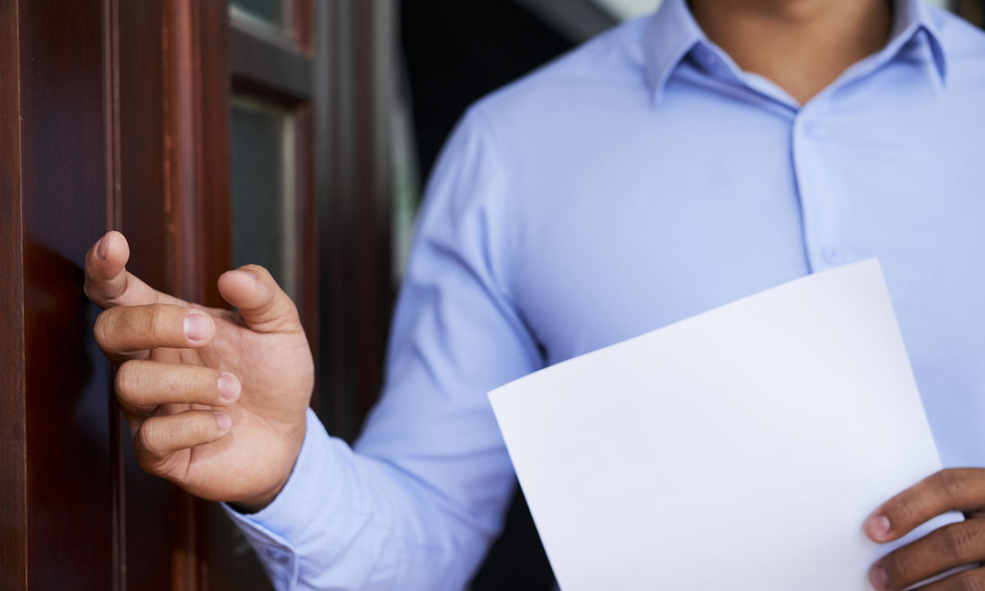 Man in blue shirt holding a paper knocking on a door