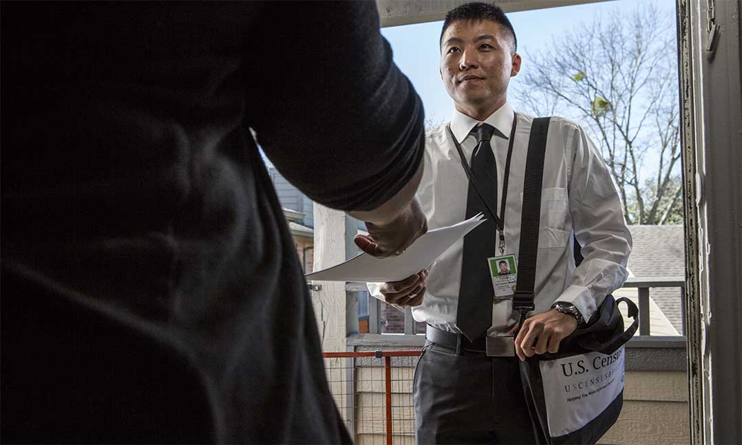 Young man hands a 2020 census paper to a woman reaching out in doorway 