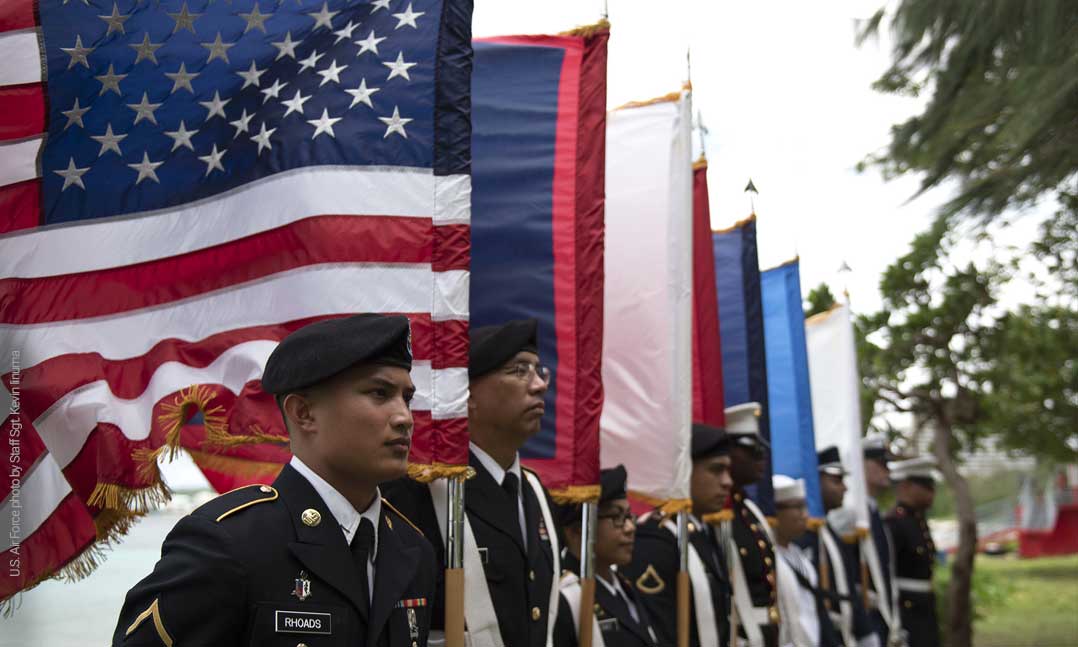 A joint color guard stands in front of flags