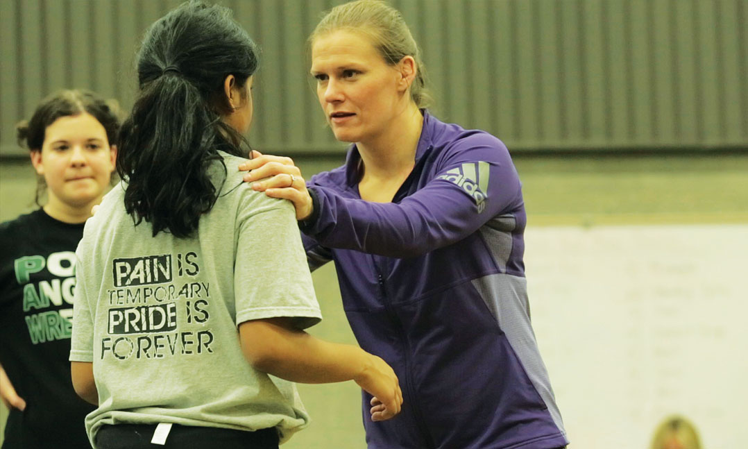 Wrestle Like a Girl founder Sally Roberts works with a young woman on the wrestling mat in 2017