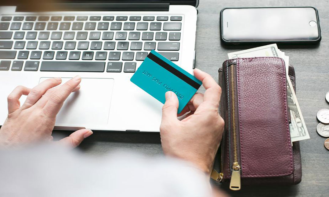 person holding a credit card in front of a laptop