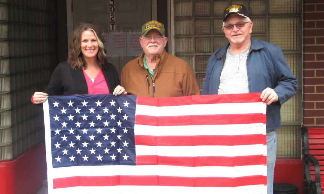 Two men and a woman hold a U.S. flag donated by the local VFW