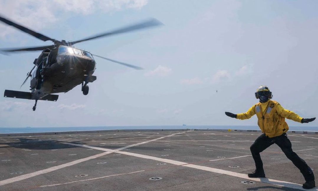 Aircrewman signals to a blackhawk landing on deck