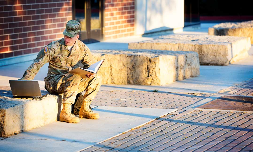 soldier going to school with laptop and book sitting on the steps